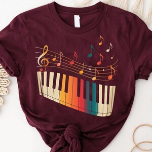 A burgundy t-shirt with a colorful graphic design depicting a piano keyboard and musical notes.