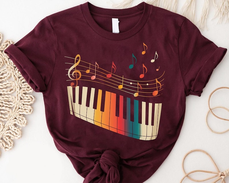 A burgundy t-shirt with a colorful graphic design depicting a piano keyboard and musical notes.