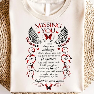 May include: White t-shirt with a black and red design featuring a pair of angel wings, a butterfly, and the text "MISSING YOU". The text reads "I think about you always. I think about you still. You have never been forgotten. And you never will. I hold you close within my heart. And there you will remain to walk with me throughout my life... Until we meet again."