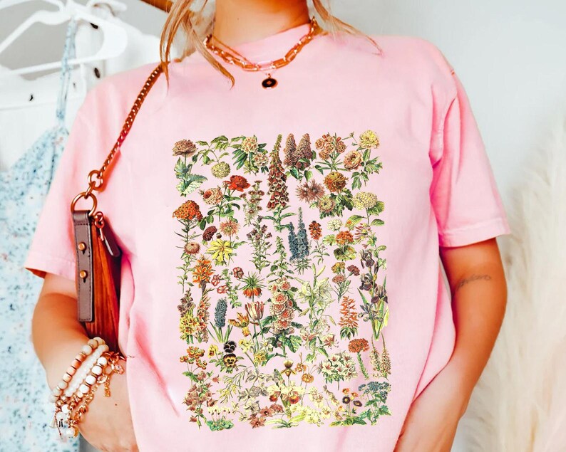 A person wearing a pink t-shirt with a floral print, standing in front of a clothing rack with various garments hanging.