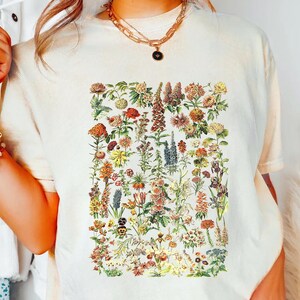 A person wearing a white t-shirt with a colorful floral print, accessorized with multiple bracelets and a necklace.