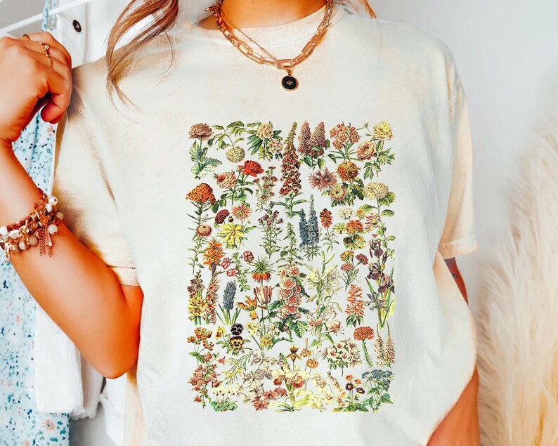 A person wearing a white t-shirt with a colorful floral print, accessorized with multiple bracelets and a necklace.