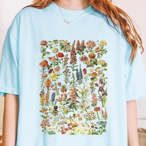 A person wearing a light blue t-shirt with a colorful graphic of various flowers and plants printed on it.