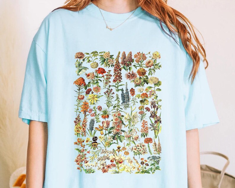 A person wearing a light blue t-shirt with a colorful graphic of various flowers and plants printed on it.