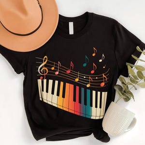 a black t-shirt with a colorful graphic design of a piano keyboard and musical notes, along with a beige hat and a white mug.