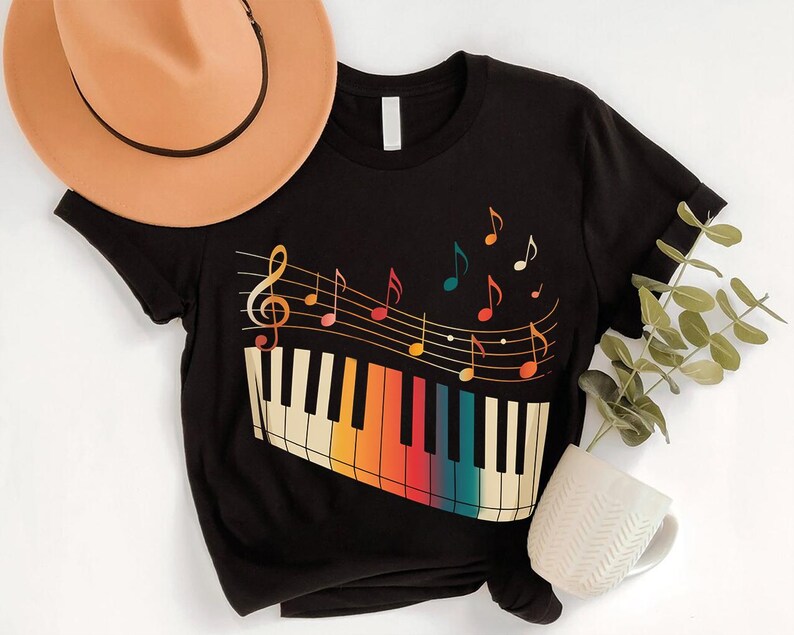 a black t-shirt with a colorful graphic design of a piano keyboard and musical notes, along with a beige hat and a white mug.