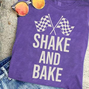 A purple t-shirt with the text "SHAKE AND BAKER" printed on it, along with a pair of sunglasses and a pair of jeans.