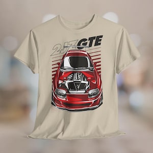 Könnte beinhalten: Beiges T-Shirt mit roter Sportwagen-Grafik und dem Text "2JZ GTE". Das Auto ist mit geöffneter Motorhaube dargestellt, die den Motor zeigt. Das Design beinhaltet rote und weiße Streifen.
