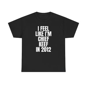 以下が含まれることがあります： 白い文字で「I FEEL LIKE I'M CHIEF KEEF IN 2012」と書かれた黒いTシャツ。Tシャツは半袖で、クルーネックです。テキストはシャツの前面の中央に配置されています。