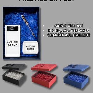 May include: A blue gift box with a white power bank, a pen, and a small round container. The power bank has a digital display showing "100". The pen and container have the text "Custom Brand". The box is open and the items are visible. The text "PRESTIGE GIFT SET" is above the box. Below the box, there are three boxes in different colors: black, red, and blue.