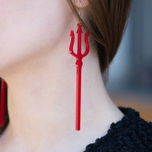 May include: A pair of long, red, acrylic earrings shaped like a trident.