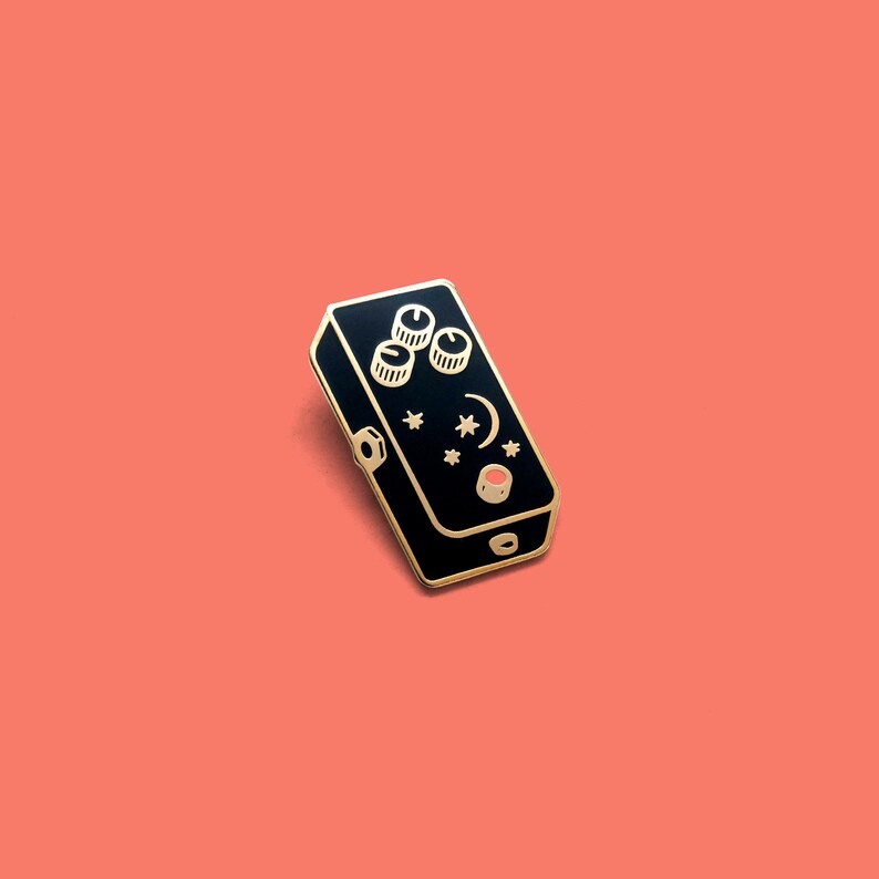 May include: A black metal guitar pedal with gold knobs and a red button. The pedal has a crescent moon and stars design.