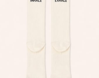 Peut inclure: Deux chaussettes côtelées blanc cassé avec les mots "INHALE" et "EXHALE" imprimés en noir. Les chaussettes sont présentées sur un fond beige clair. Chaussettes décontractées.