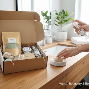 Op de afbeelding: Een bruine kartonnen doos gevuld met wellnessproducten, waaronder badzout, kleine potjes en een spuitfles. De doos is open en staat op een houten oppervlak. De tekst "Muscle Recovery & Relaxation Ritual" is zichtbaar.