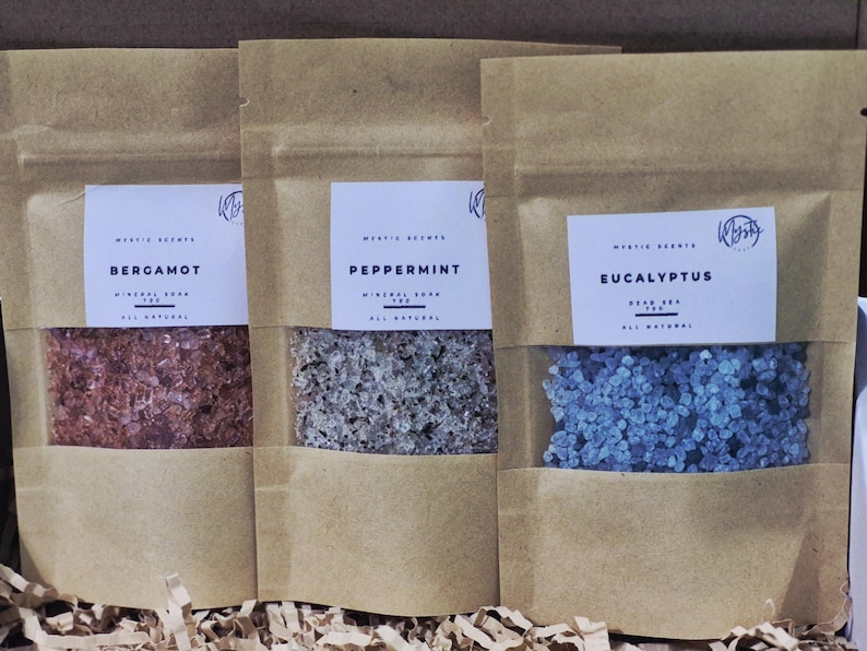 May include: Three kraft paper pouches with clear windows, each containing mineral soap. The pouches are labeled "Bergamot," "Peppermint," and "Eucalyptus." The soap crystals are red, gray, and blue, respectively. The text "Mystic Scents" is visible.