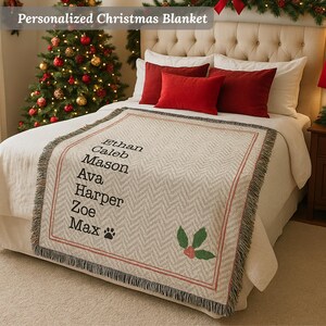 May include: A personalized Christmas blanket with a herringbone pattern, fringed edges, and a red border. The blanket features names in black text and a holly design. Red pillows and a Christmas tree are in the background.