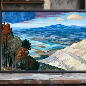 May include: Landscape painting in a black frame. The artwork depicts a valley with mountains in the background, a blue sky with clouds, and trees with orange and green foliage. The painting is displayed on a wooden table.