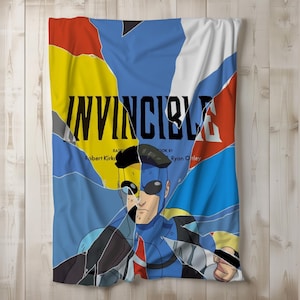 May include: A soft, folded blanket featuring a comic book-style design. The blanket displays the word "INVINCIBLE" in large black letters, with a character illustration and fragmented background in blue, yellow, red, and white.