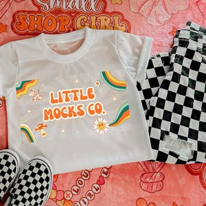 May include: White t-shirt with a rainbow graphic and the text "Little Mocks Co."