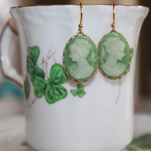 May include: A pair of green cameo earrings with gold-tone hooks. The cameos feature a white silhouette of a woman's profile.