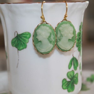 May include: A pair of green cameo earrings with gold-toned accents. The cameos feature a profile of a woman's face.