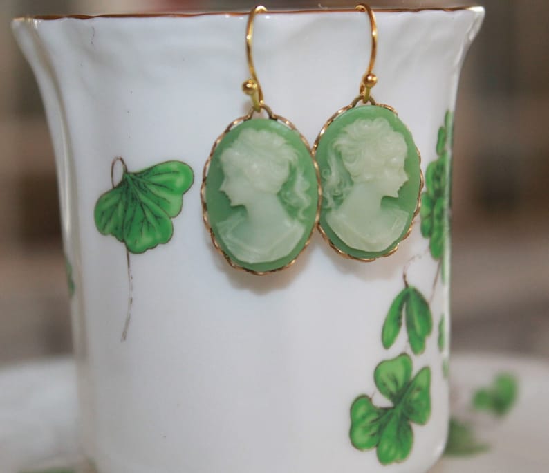 May include: A pair of green cameo earrings with gold-toned accents. The cameos feature a profile of a woman's face.