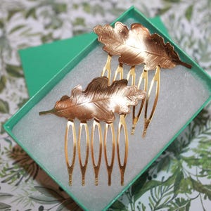 May include: Two gold leaf hair combs in a teal box. The combs are shaped like oak leaves and have a gold finish.