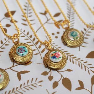 May include: Five gold necklaces with floral locket pendants. Each locket has a different floral design with white, blue, and pink flowers.