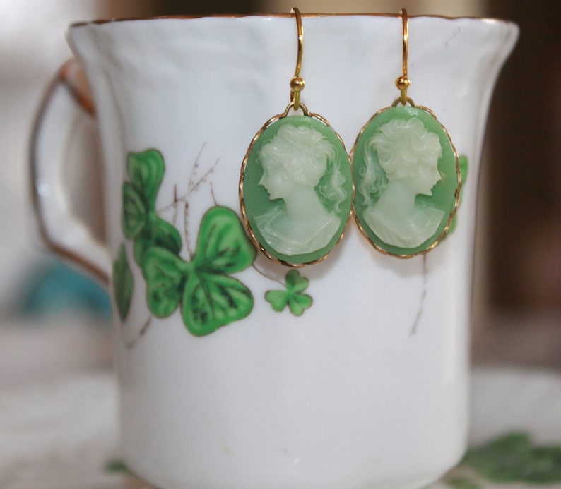 May include: A pair of green cameo earrings with gold-tone hooks. The cameos feature a white silhouette of a woman's profile.