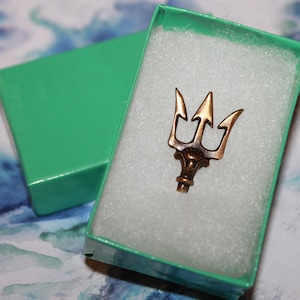 May include: A bronze trident charm in a teal gift box with white foam padding.