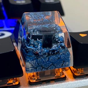 Puede incluir: Una tecla de teclado personalizada con un diseño de dragón azul y blanco encapsulado en resina transparente. La tecla está iluminada por luces naranjas del teclado. Un accesorio único para teclados mecánicos.