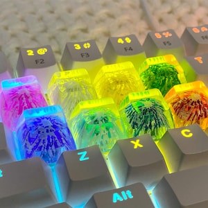 Puede incluir: Un teclado mecánico blanco con teclas de colores. Las teclas son translúcidas y tienen un patrón de remolino en el interior. Las teclas son para las teclas F1 a F6, Z, X, C y V.