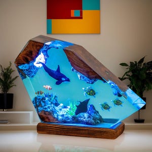 May include: A striking resin sculpture with an underwater theme. It features a blue orca, clownfish, sea turtles, and a manta ray encased in clear, blue resin. The wooden frame and base provide a natural contrast to the marine life. The sculpture is a decorative piece.