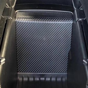 May include: Black car console with a carbon fiber pattern insert. The console is open, revealing the storage compartment. The interior has a textured, patterned design. The console is surrounded by black leather.