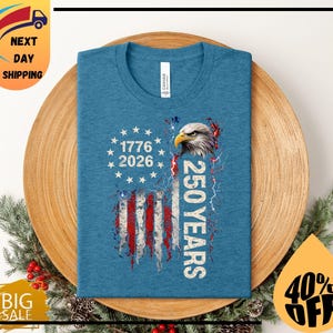 Pode incluir: Uma camiseta azul com um design desgastado da bandeira americana, uma &aacute;guia e o texto "1776 2026 250 YEARS". A camisa &eacute; feita de um material macio.