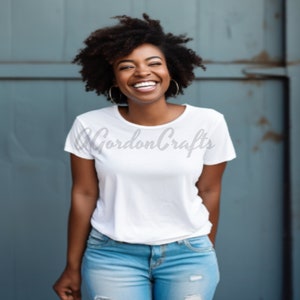 May include: A woman with curly black hair is wearing a white t-shirt with the text "Gordon Crafts" printed on it. She is smiling and wearing blue jeans.