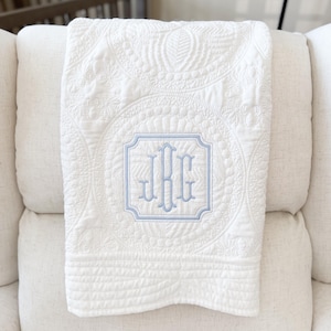 May include: White quilted baby blanket with a blue embroidered monogram "JBG" in a decorative frame.