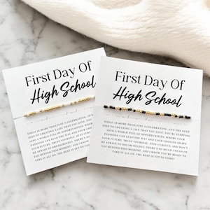 Peut inclure: Deux cartes blanches avec le texte "First Day Of High School" en écriture noire. Chaque carte comporte un bracelet de perles avec des perles dorées, noires et blanches. Les cartes contiennent également un texte inspirant sur l'avenir.