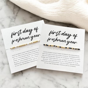 Peut inclure: Deux cartes blanches avec le texte "first day of freshman year" en écriture noire. Chaque carte comporte un bracelet de perles avec des perles dorées, noires et blanches. Les cartes ont un texte inspirant en dessous.