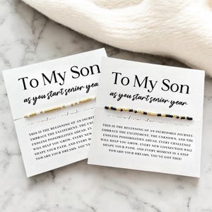 May include: Two white cards with the text "To My Son as you start senior year". Each card has a beaded bracelet. One bracelet has gold and white beads, the other has black and gold beads. The cards have inspirational text.