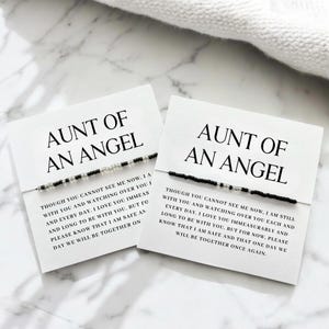 Peut inclure: Deux cartes blanches avec le texte "AUNT OF AN ANGEL" et un bracelet de perles. Les cartes contiennent un message sur l'amour et les retrouvailles. Les bracelets ont des perles noires et argentées.