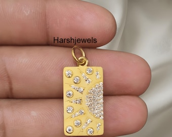 May include: A gold-coloured rectangular pendant with a sun design. The sun is made of small, sparkling stones. The pendant has a small loop at the top for a chain. The text "Harshjewels" is visible.