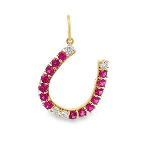 Puede incluir: Colgante de herradura dorado con piedras rojas y diamantes blancos. El colgante tiene un pequeño lazo en la parte superior para una cadena. Las piedras están dispuestas en un diseño curvo. Joyería.