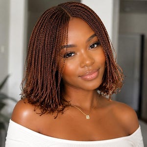 May include: A shoulder-length hairstyle featuring fine, auburn-toned micro-braids with a centre part. The hair has a glossy finish and is styled in a straight, blunt cut. A delicate gold chain necklace with a small, square pendant is visible.