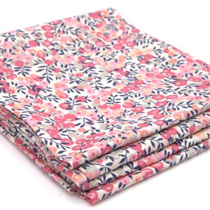 May include: A stack of folded fabric napkins with a floral pattern. The pattern features small pink and red flowers with gray and navy blue leaves on a white background. The napkins are neatly stacked.