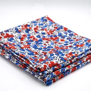 May include: A stack of folded fabric with a floral pattern in red and blue on a white background. The fabric is tightly folded, showcasing the detailed print of small flowers and leaves. The overall aesthetic is clean and bright.