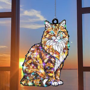 May include: A decorative cat-shaped suncatcher with a stained-glass appearance. The cat features a fluffy, multi-colored coat in shades of orange, brown, and yellow. It hangs from a silver chain, with a backdrop of a sunset over the ocean.
