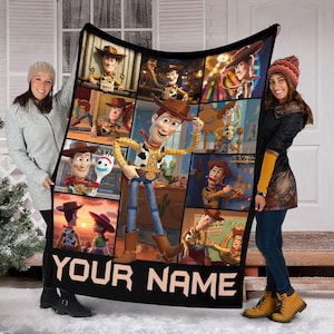 Op de afbeelding: Zwarte deken met een collage van afbeeldingen van het personage Woody uit de film Toy Story. De deken heeft de tekst "YOUR NAME" in het wit onderaan. De deken wordt door twee personen omhoog gehouden.