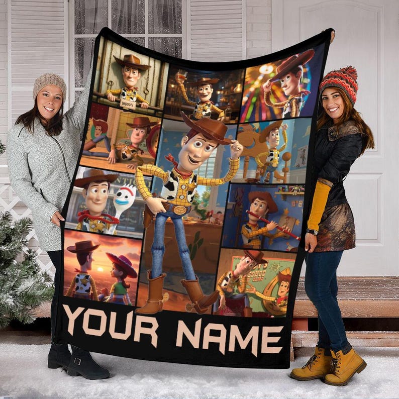 Op de afbeelding: Zwarte deken met een collage van afbeeldingen van het personage Woody uit de film Toy Story. De deken heeft de tekst "YOUR NAME" in het wit onderaan. De deken wordt door twee personen omhoog gehouden.