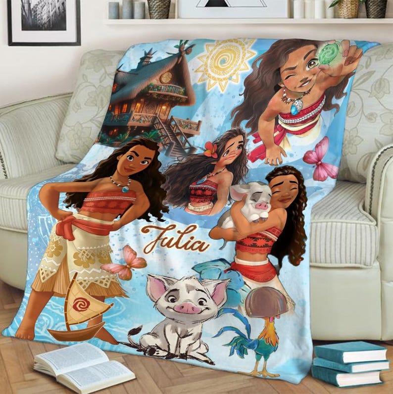 May include: A light blue fleece blanket featuring Moana characters, a small pig, a rooster, a tropical hut, and a sailboat. The name Julia is printed in brown script in the center. The design includes a yellow sun, pink butterflies, and green foliage.